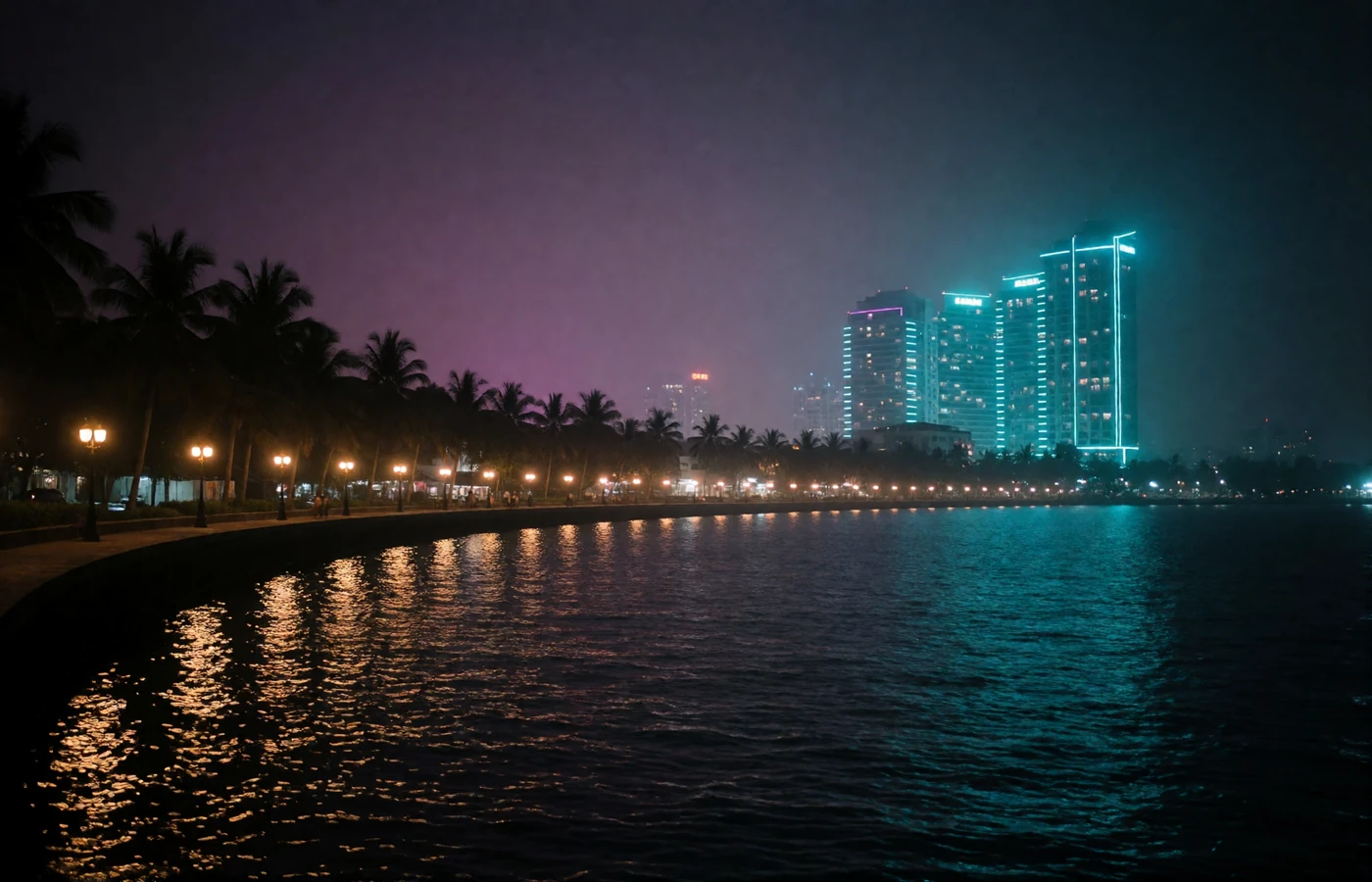 Evening view over a Philippine coastal bay with an illuminated promenade and modern towers glowing against a violet sky