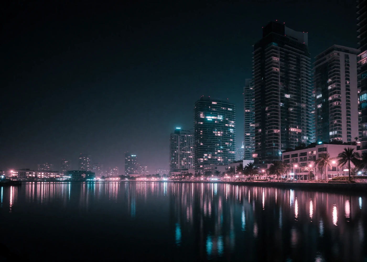 Night view across Singapore's harbour bay toward a dense cluster of illuminated modern glass towers