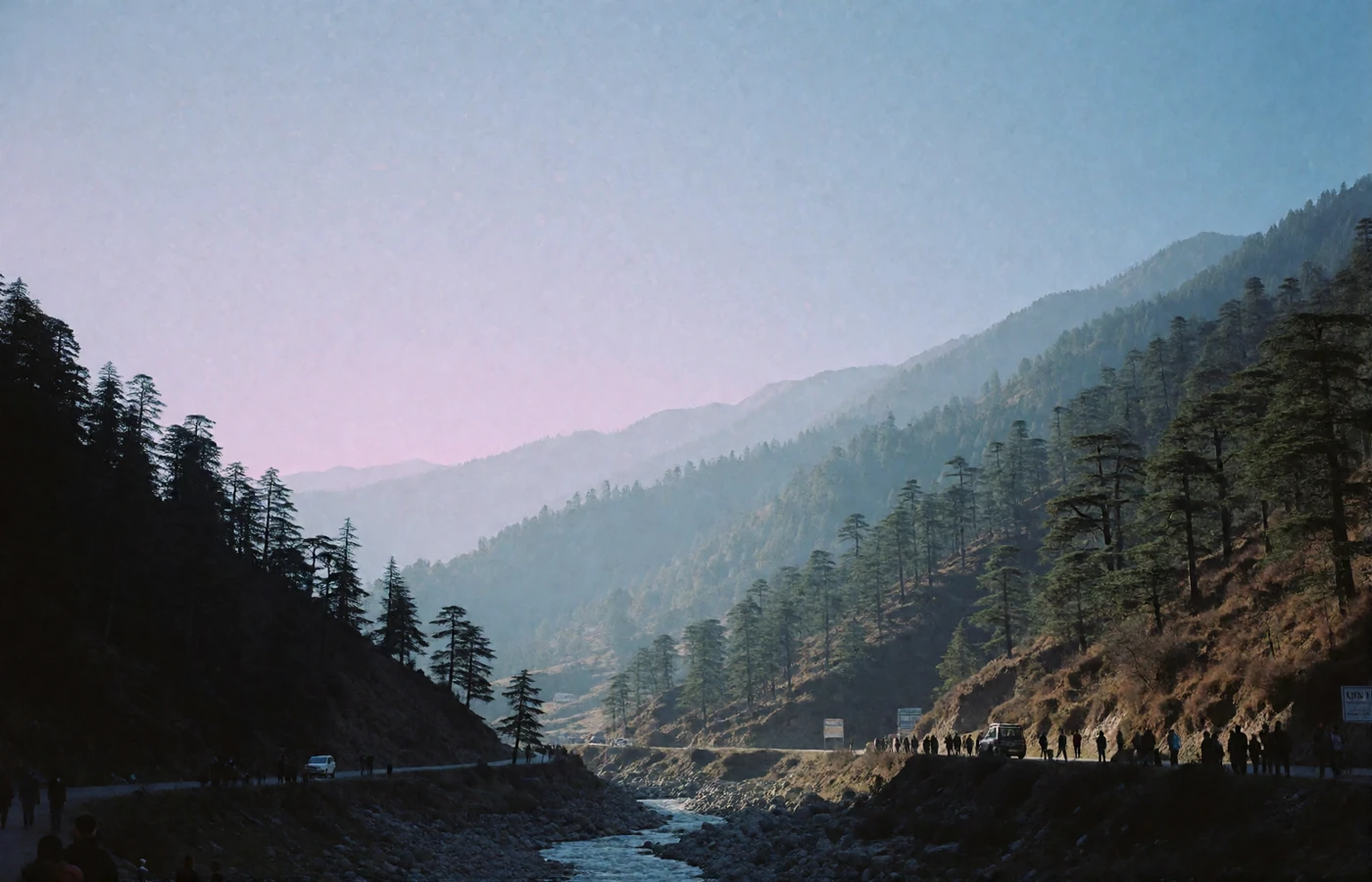 Deep Himalayan valley in Bhutan with pine-covered slopes, a winding river and layered ridgelines fading into blue haze