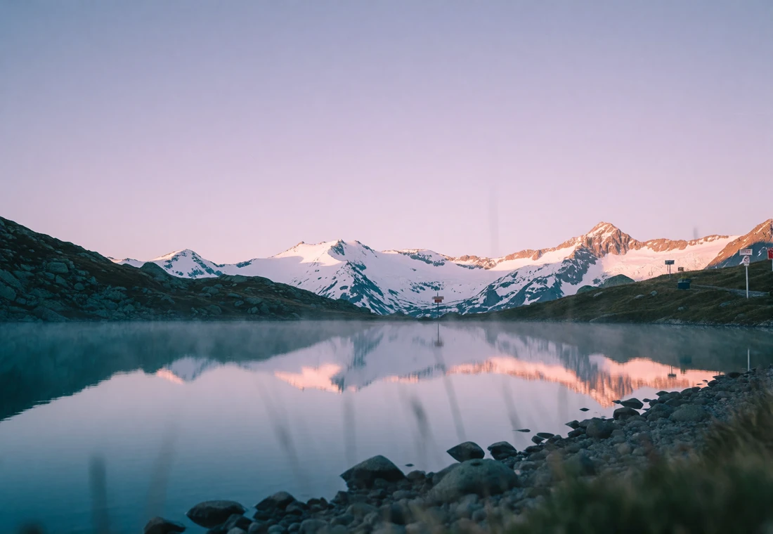 Dawn view of a high alpine lake in Kyrgyzstan reflecting snow-capped mountain ridges under a pale violet sky