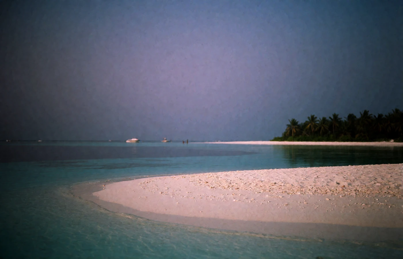 Indian Ocean atoll at dusk with a white sandbank, shallow turquoise lagoon and a palm-covered islet on the horizon