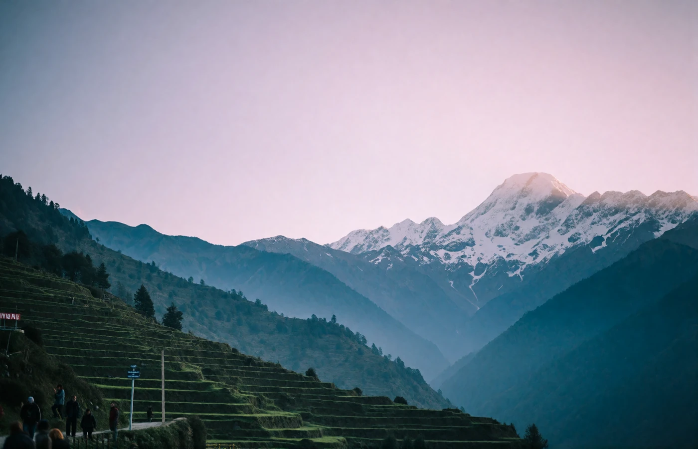 Himalayan valley in Nepal at dawn with terraced green slopes, layered blue ridgelines and a snow-capped peak on the horizon